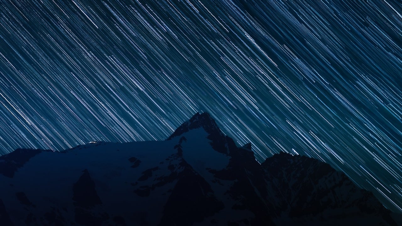 A time-lapse photo of star trails in the night sky, showing the circular motion caused by Earth's rotation. The Milky Way is visible as a bright band across the sky.